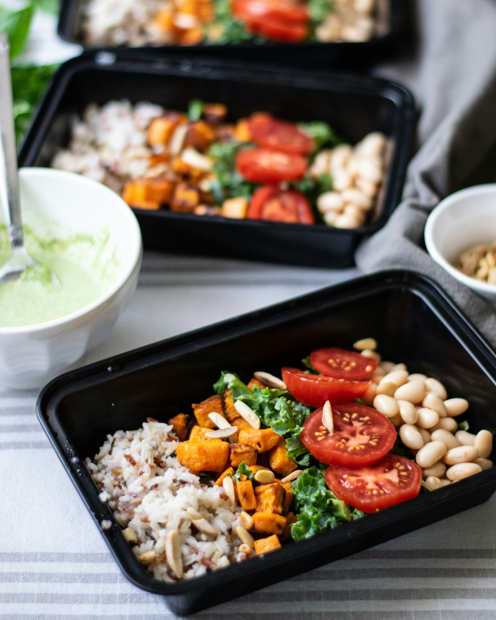 Meal prep - healthy rice, squash, kale, tomatoes and beans in tupperware on a tablecloth